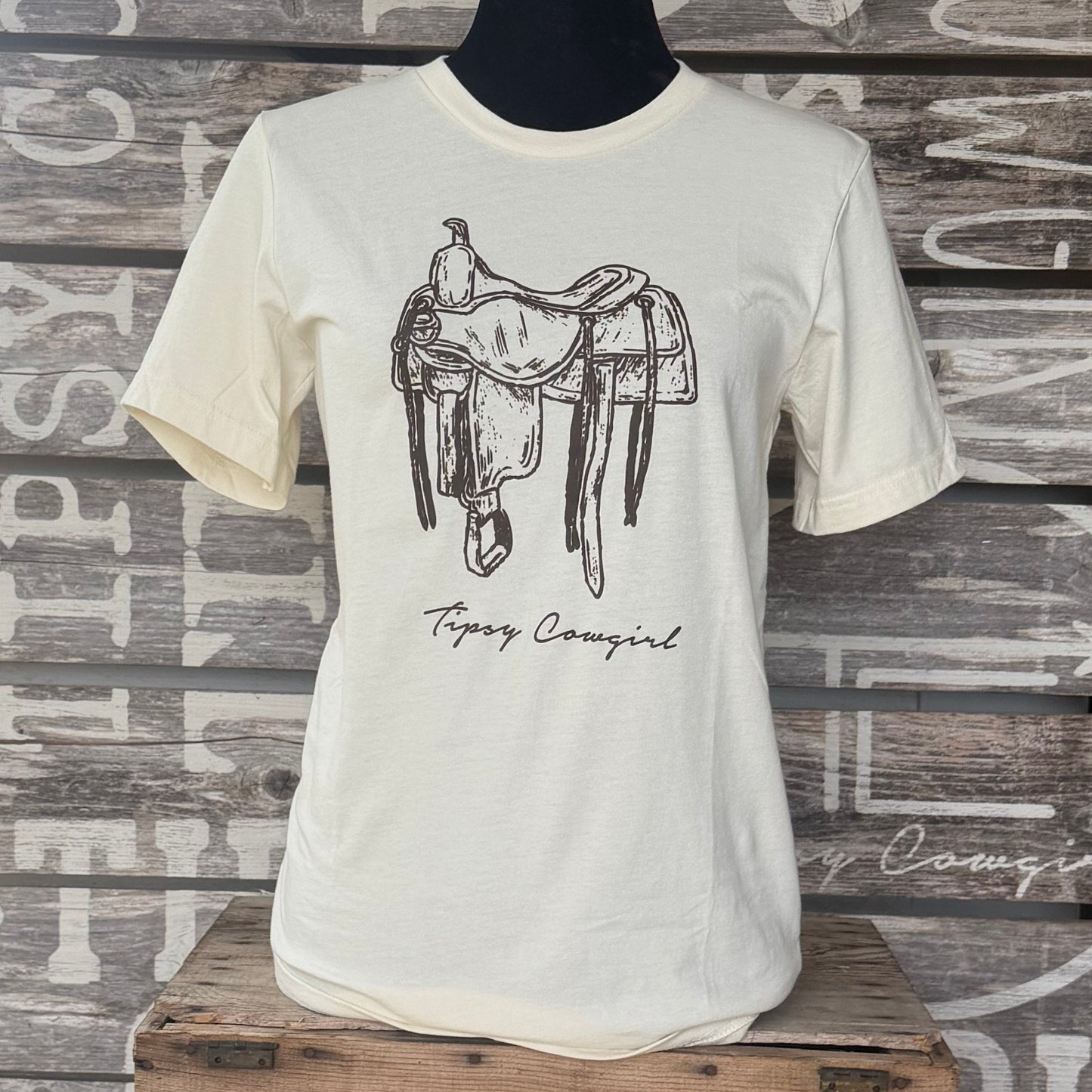 Tipsy Cowgirl The Saddle Tee in Natural featuring hand-drawn western saddle artwork and Tipsy Cowgirl signature